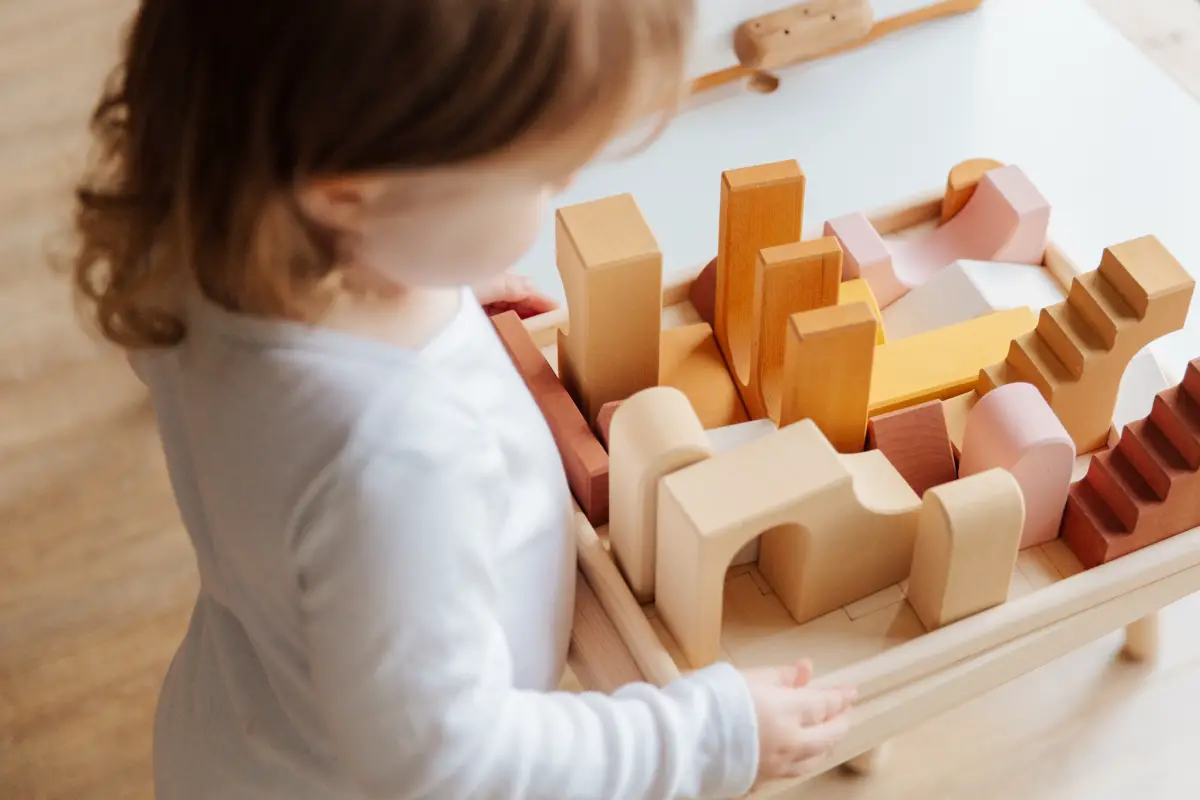 Toddler stands at a table and plays with Montessori wooden blocks