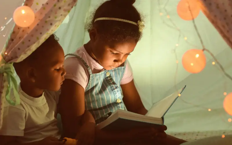 young black girl reads to her brother in a play tent