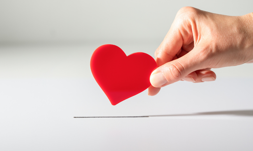 hand dropping paper heart in donation box, fundraiser