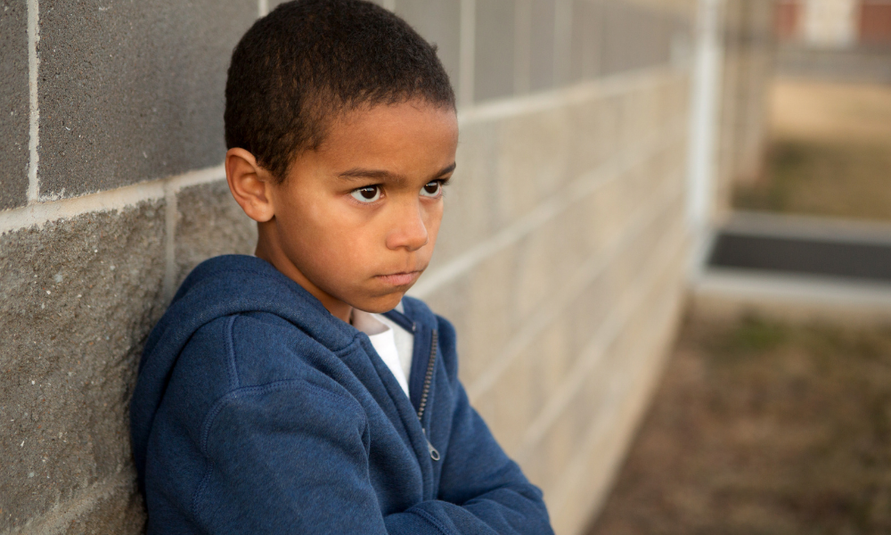 hispanic child sits alone against a cinderblock wall looking sad