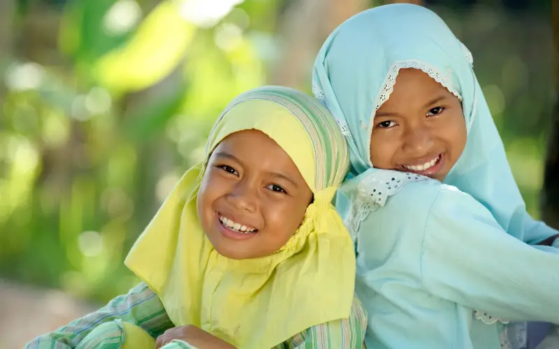two muslim girls sitting back to back smiling