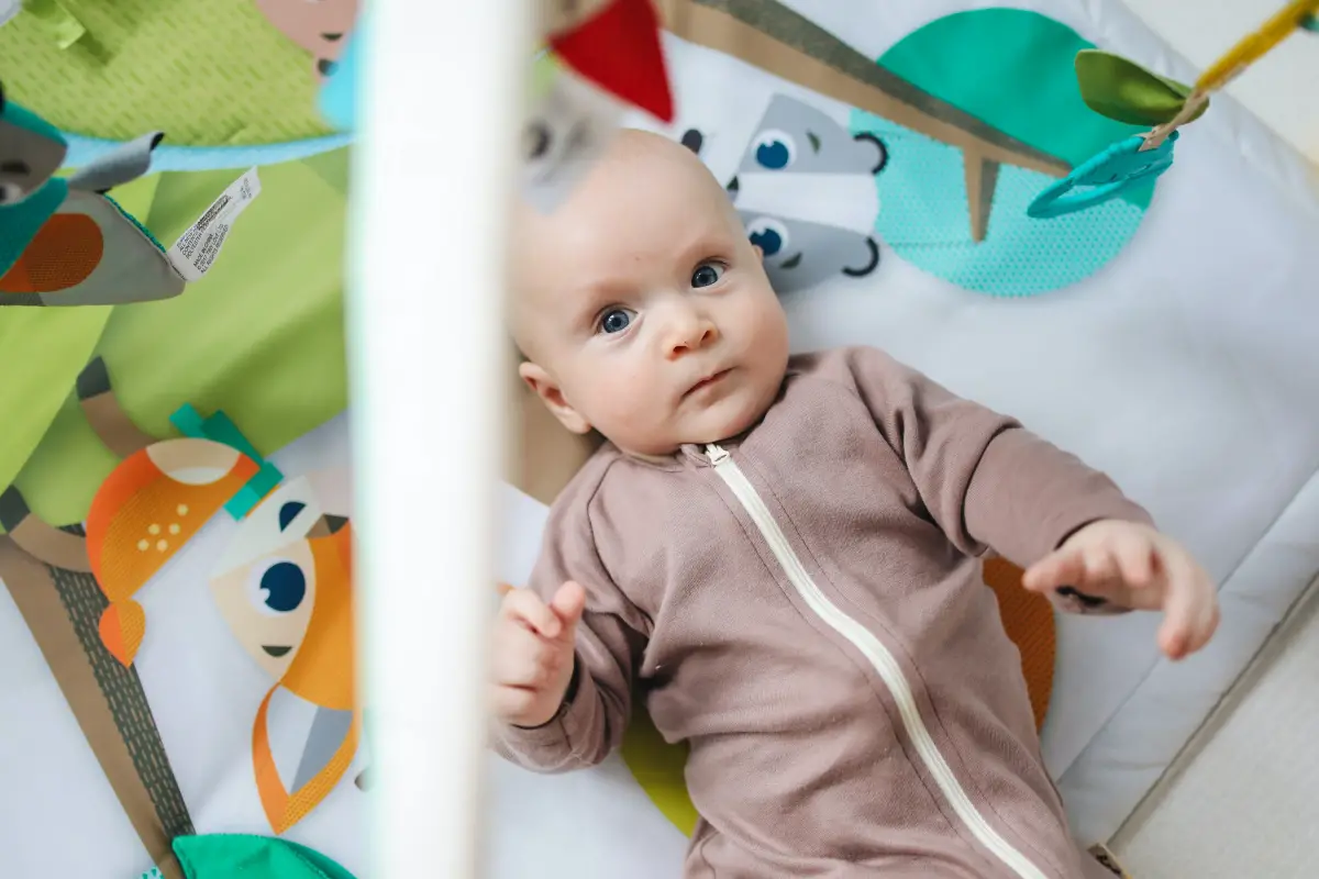 Baby lays in their crib looking up at a hanging mobile.