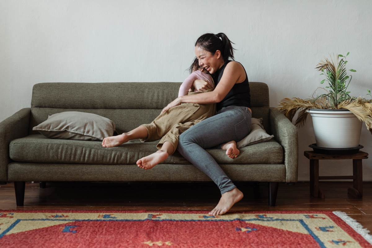 Mom sits on a couch and hugs her daughter as they laugh.