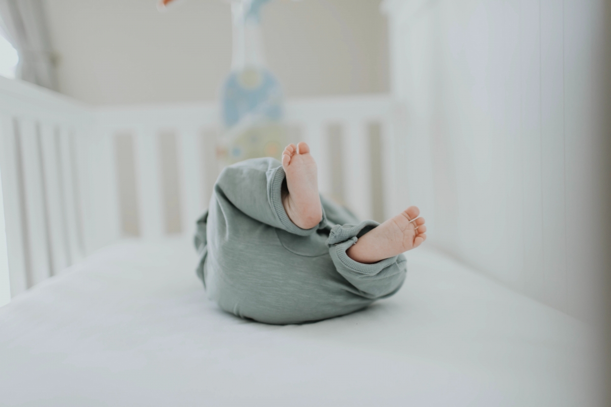 Baby kicks their feet as they lay in their crib looking up at a hanging mobile.